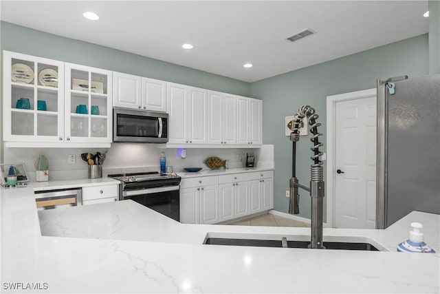 kitchen with backsplash, stainless steel appliances, white cabinets, and light tile patterned flooring