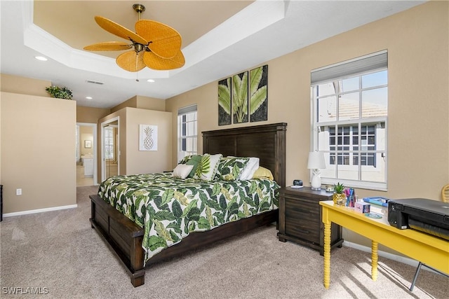 bedroom featuring ensuite bathroom, light colored carpet, ornamental molding, a raised ceiling, and ceiling fan