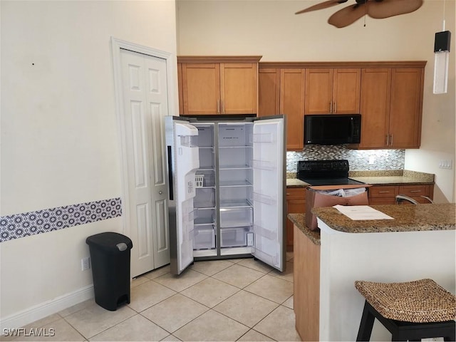 kitchen featuring a breakfast bar, electric range, freestanding refrigerator, black microwave, and brown cabinets