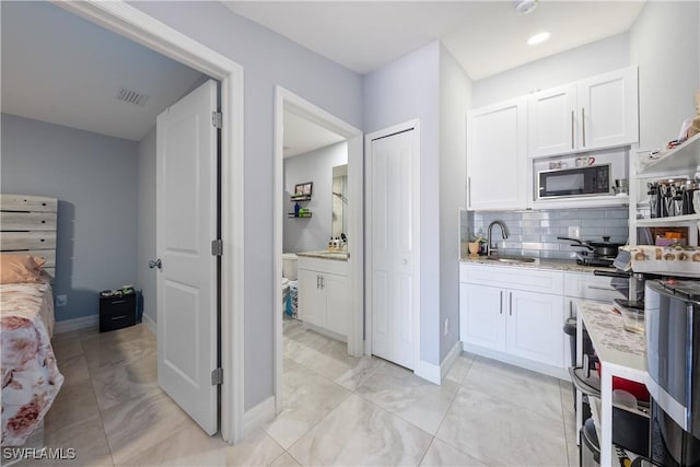 kitchen with white cabinetry, sink, backsplash, and black microwave