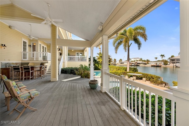 wooden terrace with a water view, ceiling fan, and an outdoor bar