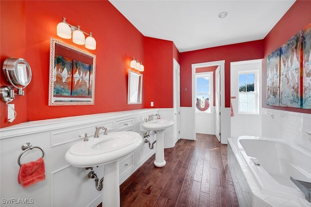 bathroom with dual sinks, wood-type flooring, and tiled bath