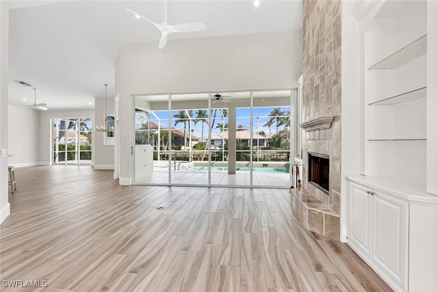 unfurnished living room featuring a high ceiling, a tile fireplace, ceiling fan, and light hardwood / wood-style flooring