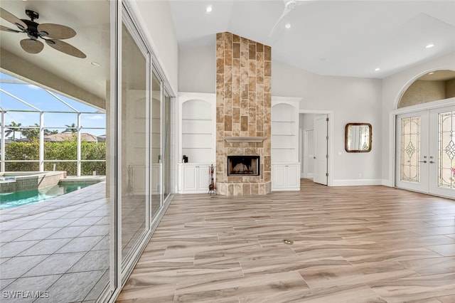 unfurnished living room featuring built in features, ceiling fan, high vaulted ceiling, a fireplace, and french doors