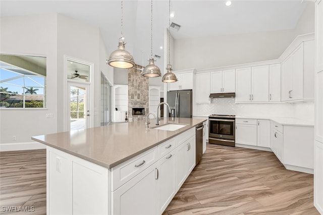 kitchen featuring sink, a kitchen island with sink, stainless steel appliances, a fireplace, and white cabinets