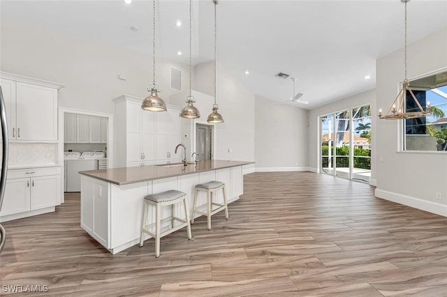 kitchen with separate washer and dryer, high vaulted ceiling, pendant lighting, a kitchen island with sink, and white cabinets