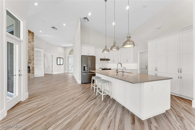 kitchen with pendant lighting, high vaulted ceiling, a spacious island, white cabinets, and stainless steel fridge with ice dispenser