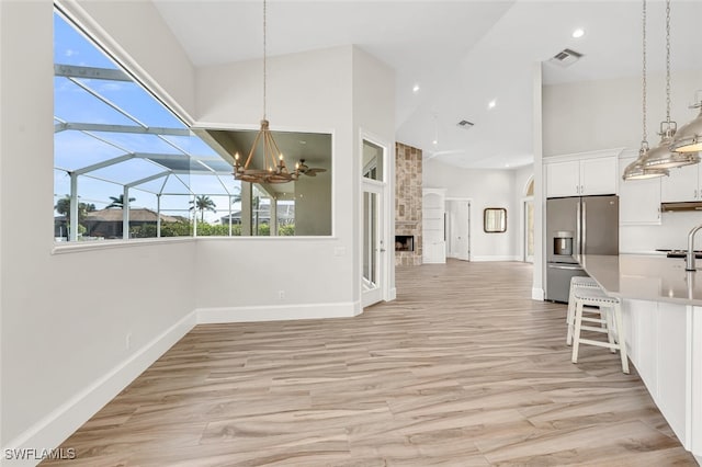 unfurnished dining area with a towering ceiling, a large fireplace, light hardwood / wood-style floors, and a notable chandelier