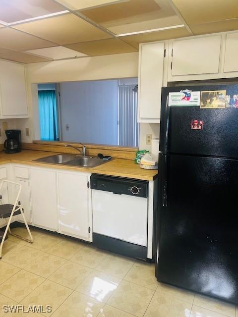 kitchen featuring black fridge, white cabinetry, white dishwasher, and sink