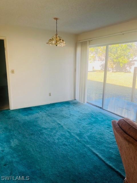 carpeted spare room featuring plenty of natural light, an inviting chandelier, and a textured ceiling