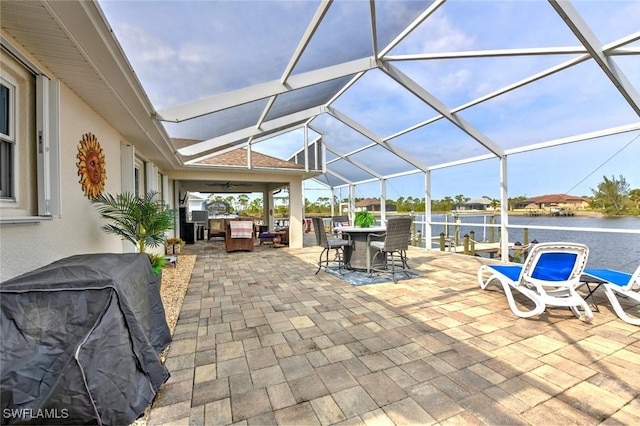 view of patio with ceiling fan, a water view, area for grilling, and glass enclosure