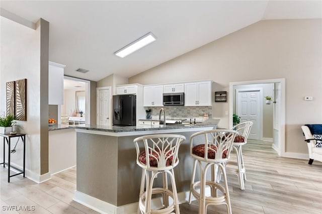 kitchen with lofted ceiling, a breakfast bar, white cabinetry, black refrigerator with ice dispenser, and decorative backsplash