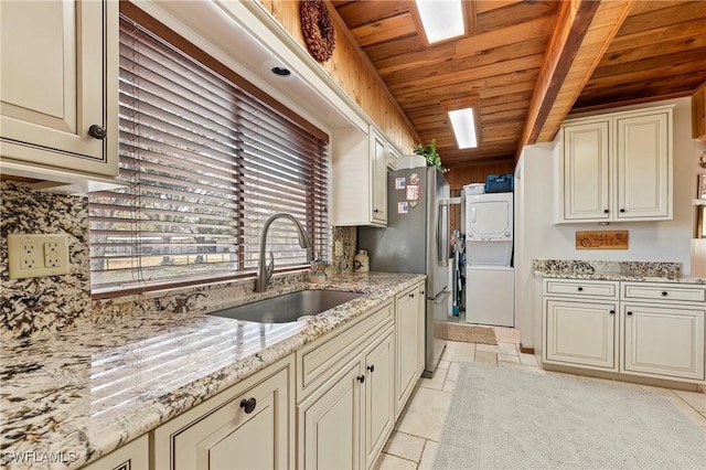 kitchen with sink, light stone counters, wooden ceiling, stacked washer / dryer, and cream cabinets