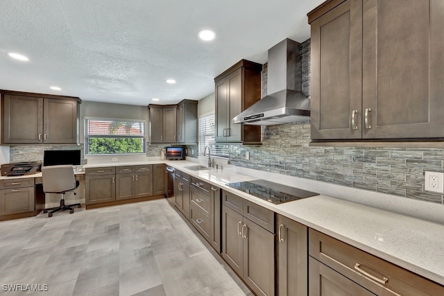 kitchen with built in desk, sink, black electric stovetop, light stone counters, and wall chimney exhaust hood