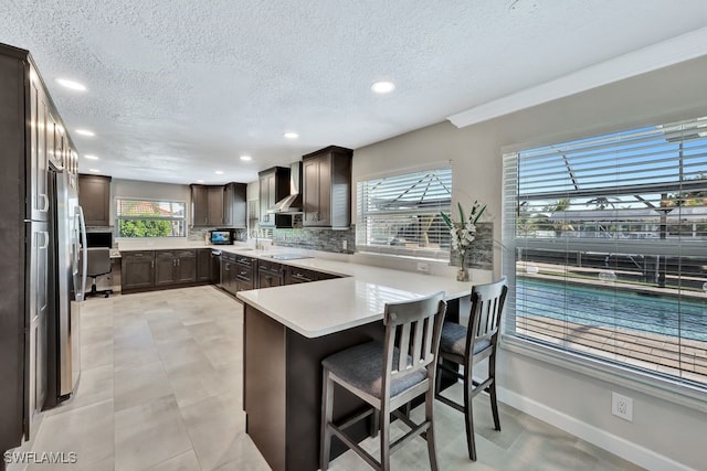 kitchen featuring wall chimney range hood, tasteful backsplash, a kitchen bar, black electric cooktop, and kitchen peninsula