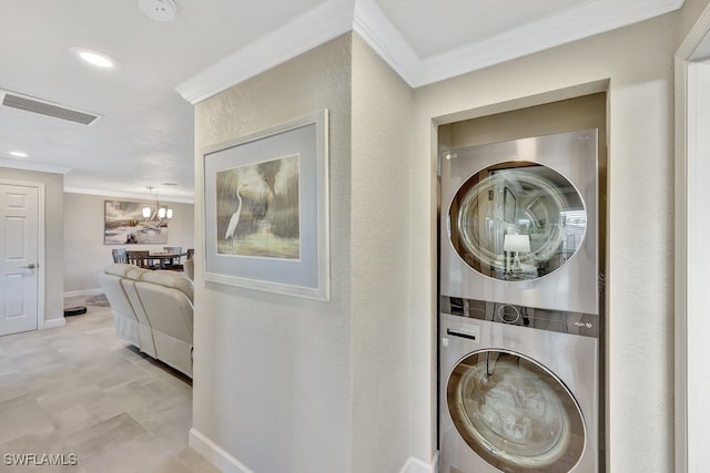 laundry room with crown molding, stacked washer / drying machine, and a notable chandelier