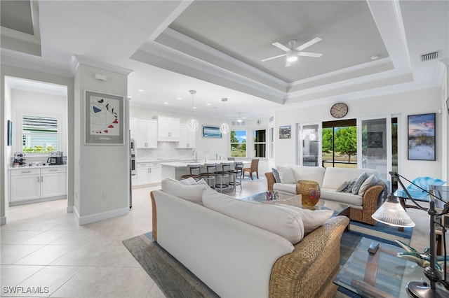 living room with visible vents, a tray ceiling, a wealth of natural light, and ornamental molding