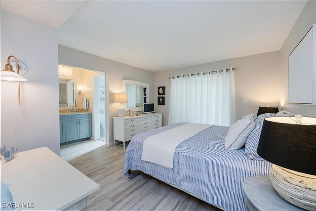 bedroom with connected bathroom, sink, and light wood-type flooring