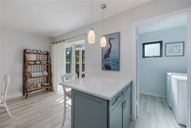 kitchen featuring a breakfast bar, washing machine and dryer, hanging light fixtures, light stone countertops, and light hardwood / wood-style floors