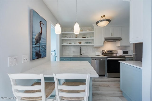 kitchen with a breakfast bar, sink, white cabinetry, hanging light fixtures, and stainless steel appliances