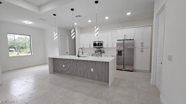 kitchen with pendant lighting, sink, appliances with stainless steel finishes, white cabinets, and a center island with sink