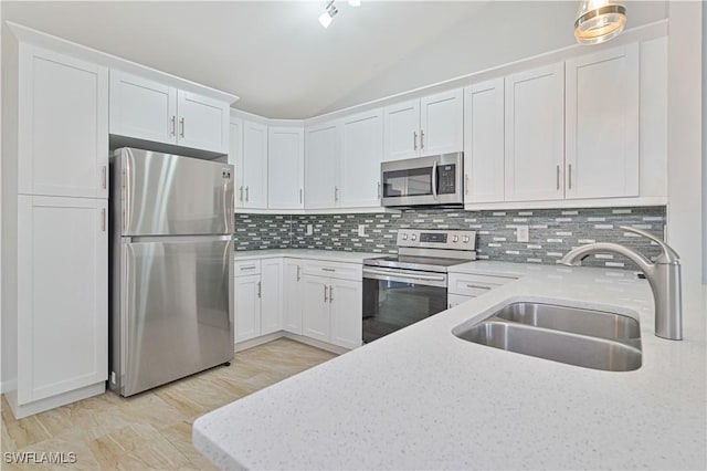 kitchen featuring stainless steel appliances, lofted ceiling, sink, and white cabinets