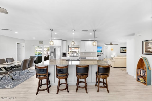 kitchen with decorative light fixtures, white cabinetry, a breakfast bar area, high end refrigerator, and light stone countertops