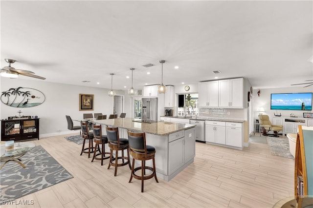 kitchen featuring a kitchen island, appliances with stainless steel finishes, white cabinetry, hanging light fixtures, and light stone countertops