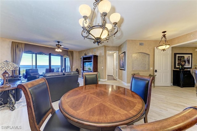 dining space featuring ceiling fan with notable chandelier, light hardwood / wood-style floors, and a water view