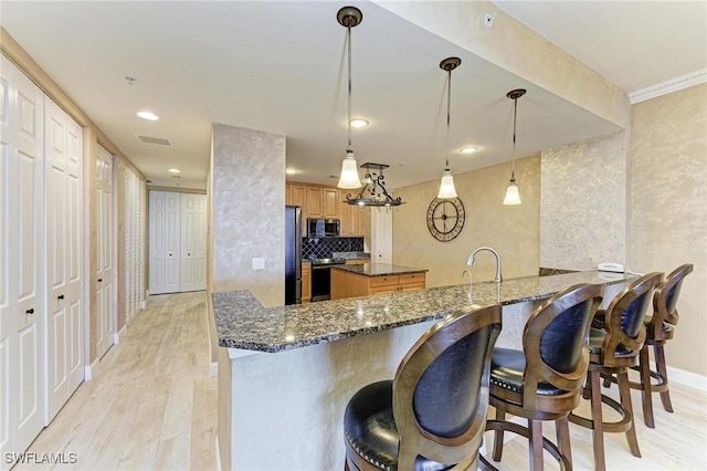 kitchen with dark stone countertops, stainless steel appliances, decorative backsplash, decorative light fixtures, and kitchen peninsula