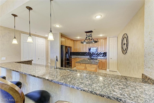 kitchen with appliances with stainless steel finishes, decorative light fixtures, dark stone countertops, and kitchen peninsula