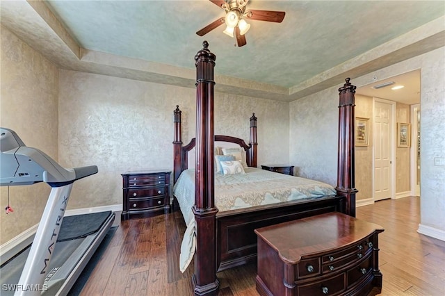 bedroom with dark wood-type flooring, ceiling fan, and a tray ceiling