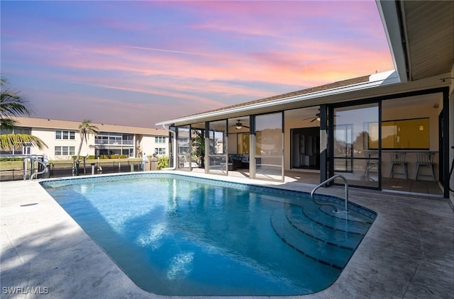 pool at dusk featuring ceiling fan and a patio area