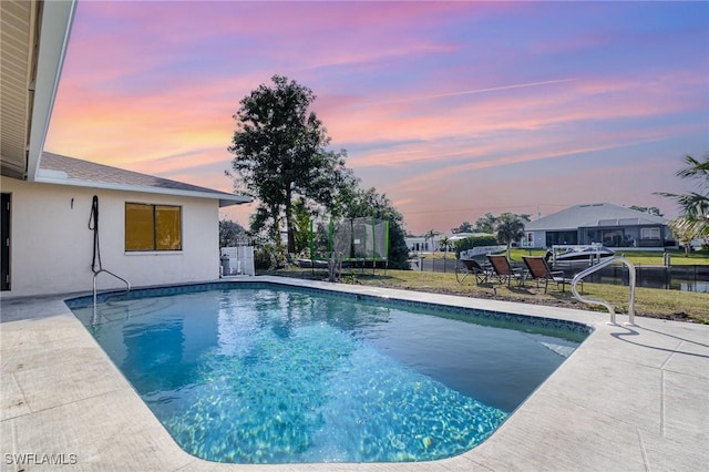 pool at dusk featuring a patio and a trampoline