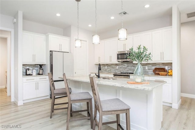 kitchen with light hardwood / wood-style flooring, white cabinetry, backsplash, hanging light fixtures, and a center island with sink