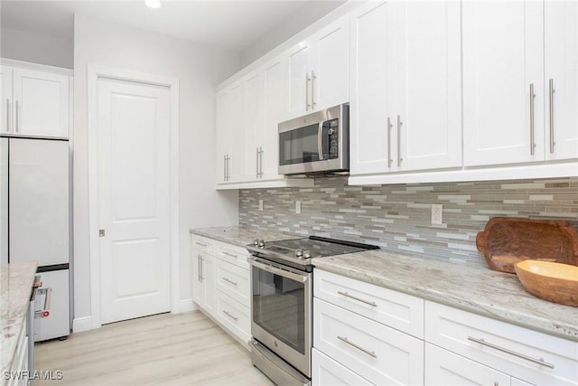 kitchen featuring white cabinetry, backsplash, stainless steel appliances, light stone countertops, and light wood-type flooring