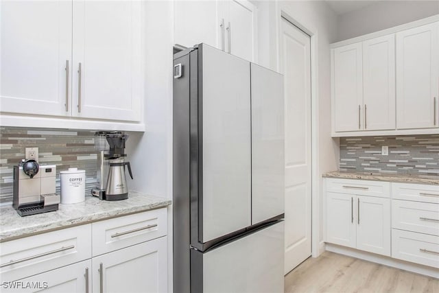 kitchen featuring refrigerator, backsplash, light stone countertops, white cabinets, and light wood-type flooring