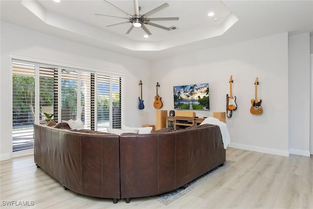 living room featuring a tray ceiling, a wealth of natural light, light hardwood / wood-style floors, and ceiling fan