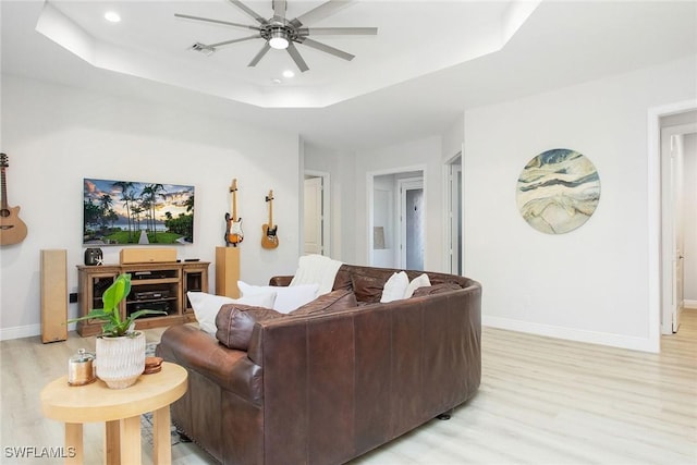 living room featuring ceiling fan, a tray ceiling, and light wood-type flooring