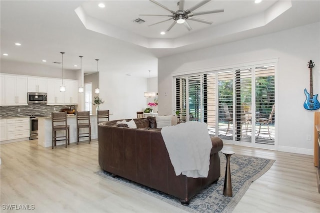 living room with ceiling fan, a raised ceiling, sink, and light hardwood / wood-style flooring