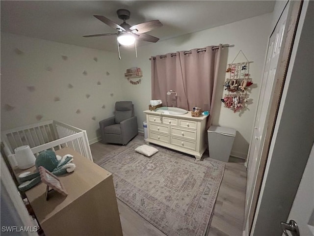 bedroom featuring ceiling fan, light hardwood / wood-style flooring, and a crib