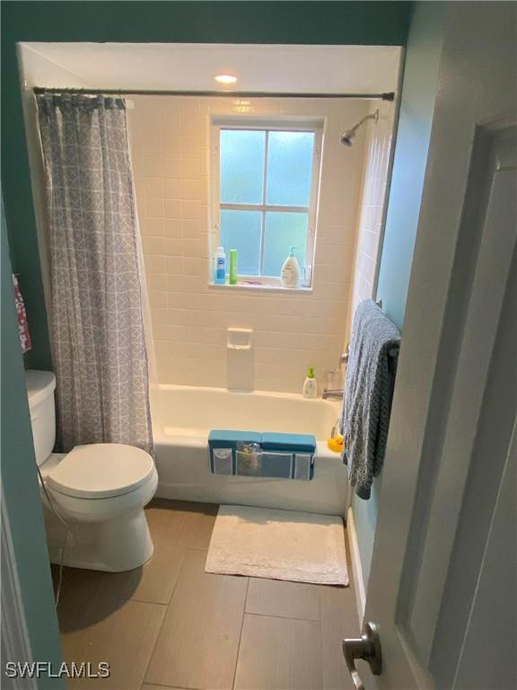 bathroom featuring tile patterned floors, toilet, and shower / bath combo with shower curtain