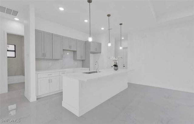 kitchen with sink, a center island with sink, gray cabinets, pendant lighting, and backsplash