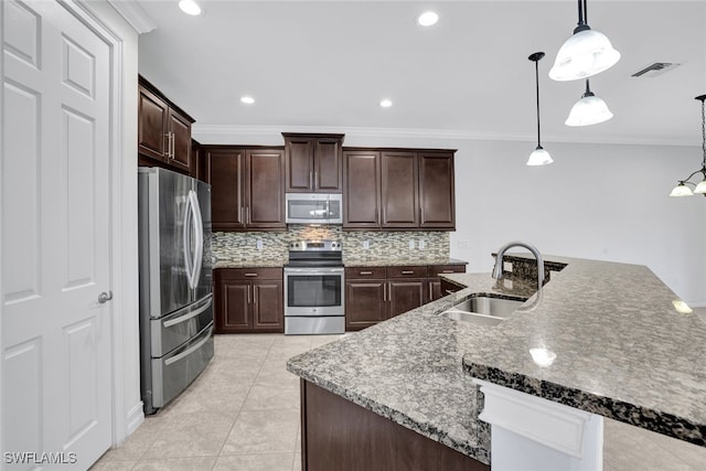 kitchen with decorative light fixtures, an island with sink, sink, backsplash, and stainless steel appliances