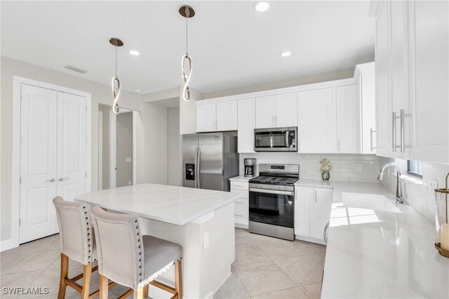 kitchen featuring stainless steel appliances, white cabinetry, hanging light fixtures, and a center island