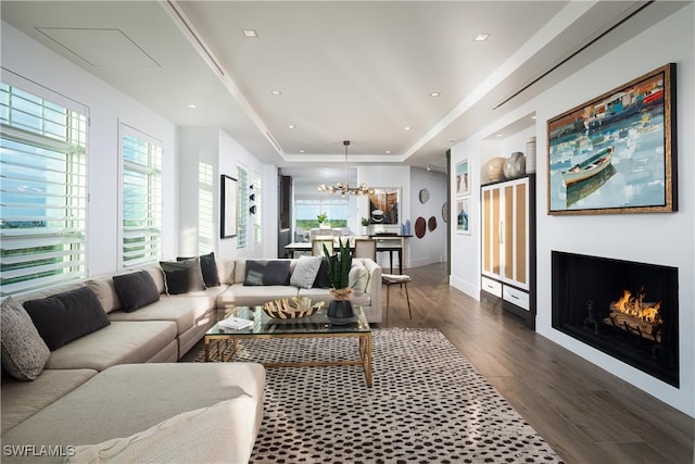 living room with dark wood-type flooring, a notable chandelier, and a tray ceiling