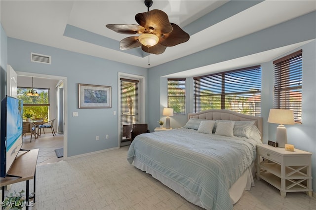 bedroom featuring ceiling fan, a tray ceiling, and multiple windows