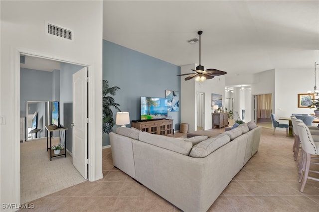 tiled living room with ceiling fan with notable chandelier and high vaulted ceiling