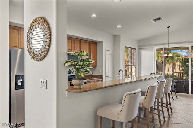 kitchen featuring light tile patterned flooring, decorative light fixtures, dark stone countertops, a kitchen breakfast bar, and stainless steel appliances