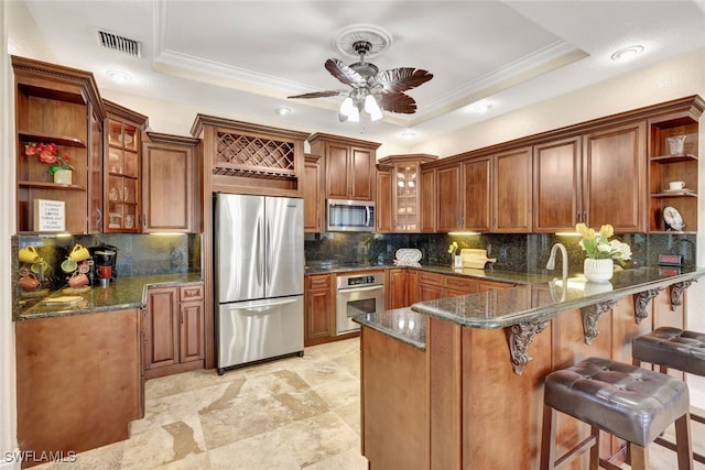 kitchen with a tray ceiling, kitchen peninsula, dark stone counters, and appliances with stainless steel finishes